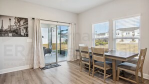 Un comedor con mesa y sillas, una puerta corredera de vidrio que da a un balcón, y vista panorámica de la ciudad.