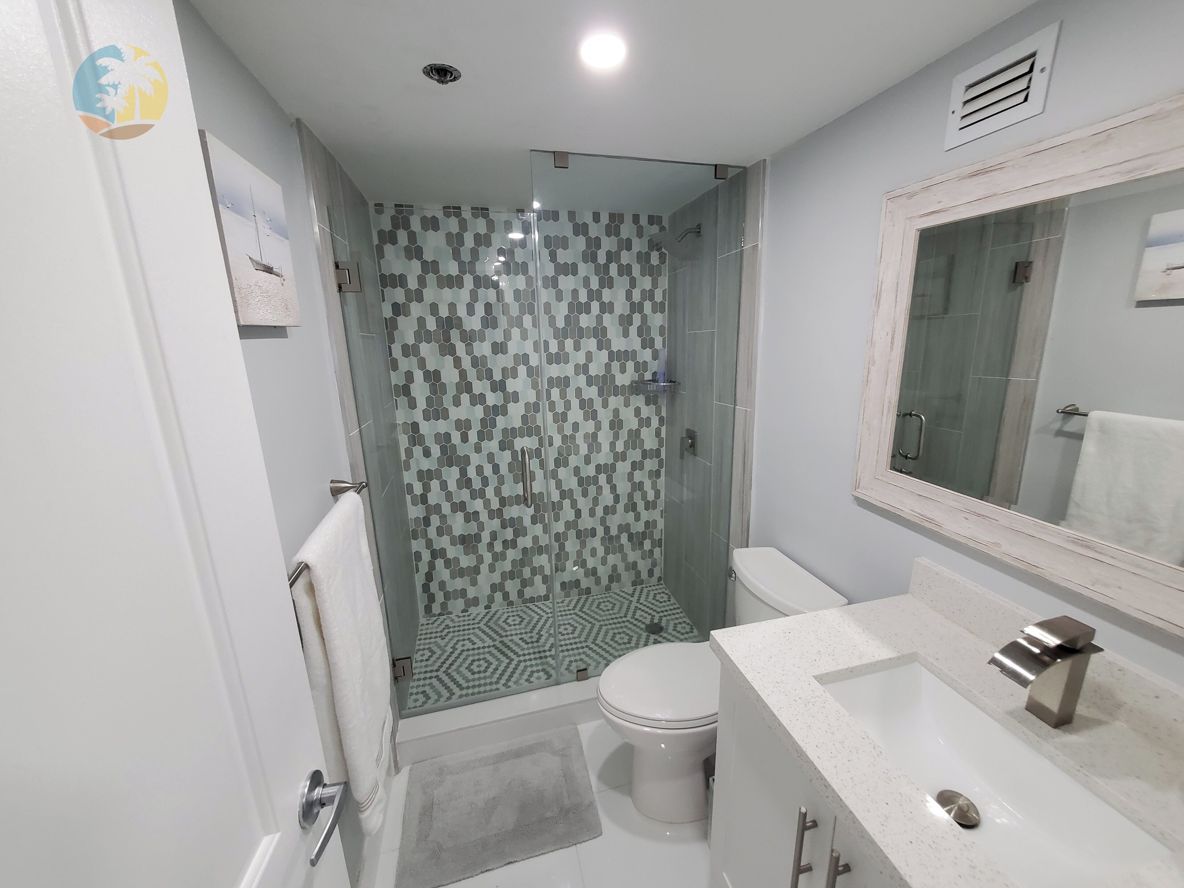 A bathroom with a glass-enclosed shower, a toilet, and a sink with a mirror.
