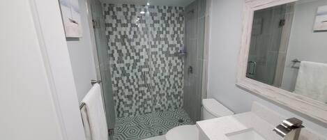 A bathroom with a glass-enclosed shower, a toilet, and a sink with a mirror.
