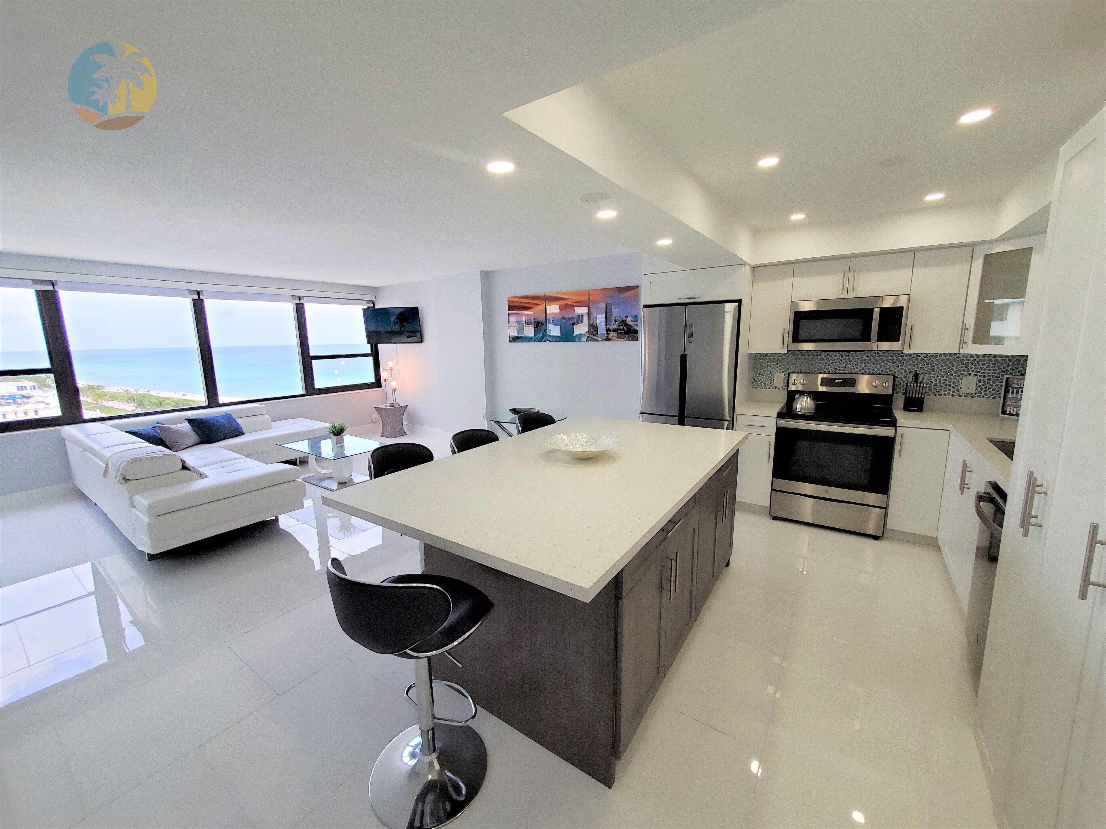 A modern kitchen with a large island, stainless steel appliances, and a view of the ocean.