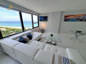 Een moderne woonkamer met een witte bank, een glazen salontafel en uitzicht op het strand.
