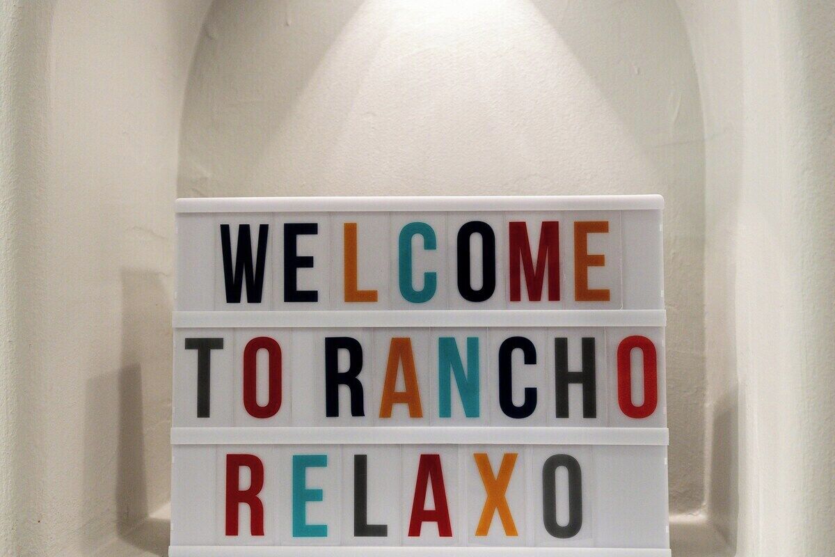 Ein Willkommensschild mit bunten Buchstaben, auf dem 'WELCOME TO RANCHO RELAXO' steht.