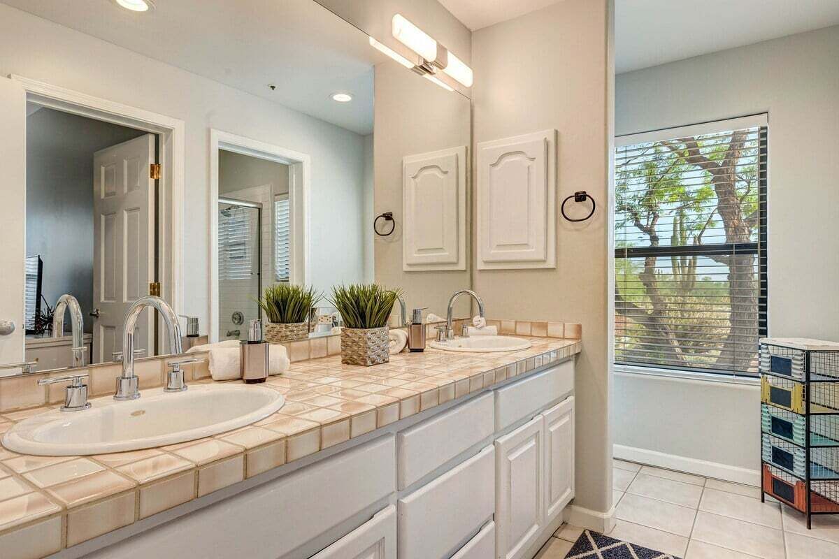 A bathroom with two sinks, a large mirror, and a window with blinds.