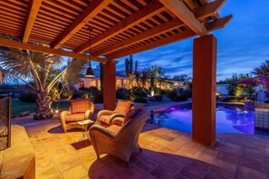 Un espacio exterior techado con piscina, dos sillones de mimbre y una pérgola.