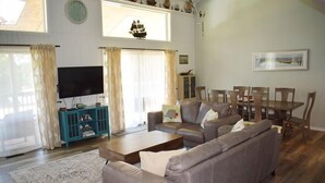 Una sala de estar con un sofá seccional, una mesa de centro, un televisor y un comedor con sillas y una mesa.