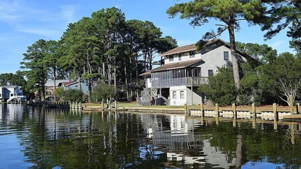 Propiedad frente al lago con una casa grande que tiene balcón, rodeada de árboles y un lago tranquilo.