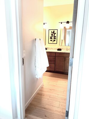 A hallway leading to a bathroom with wooden flooring, a sink, and a towel hanging on the wall. - New! Beautifully appointed 3-bedroom townhome 30 min from Purdue - Remington IN (Remington)