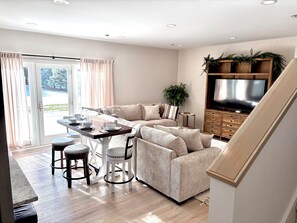 A modern living room with a sofa, a dining table with chairs, a TV, and a staircase. - New! Beautifully appointed 3-bedroom townhome 30 min from Purdue - Remington IN (Remington)