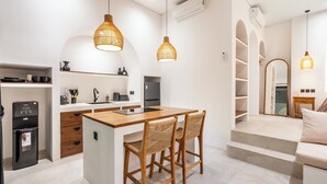 Una cuina moderna amb una illa central, dues cadires de vimet i il·luminació penjant.