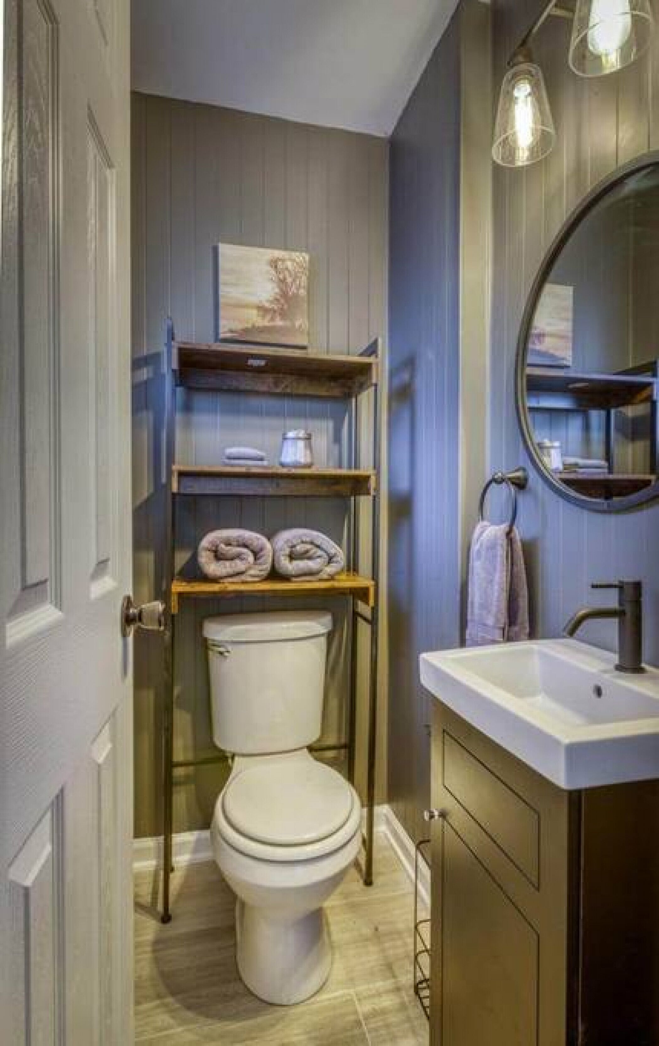 Un baño con inodoro, lavabo y repisas sobre el inodoro.