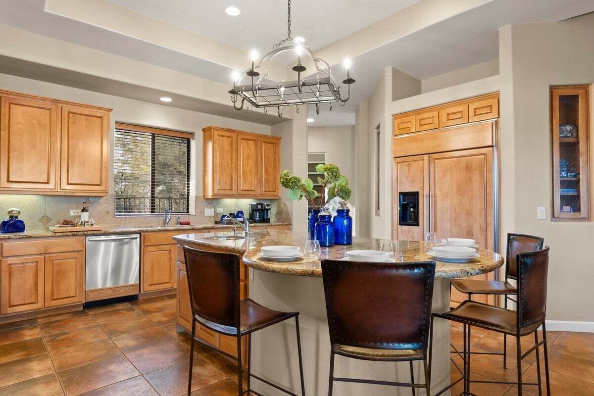 A spacious kitchen with wooden cabinets, a central island with bar stools, and a chandelier.