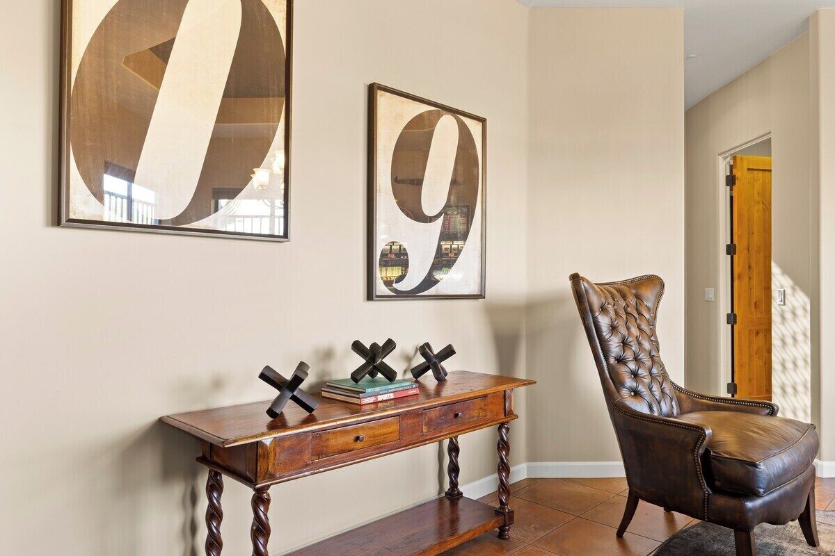 Una habitación con una consola de madera, un sillón de cuero y dos cuadros abstractos en la pared.