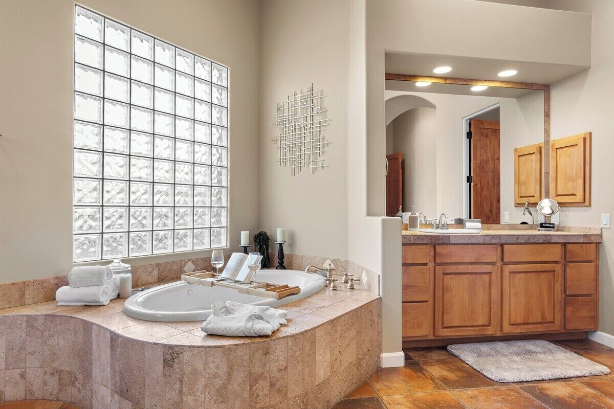 A modern bathroom with a large window, a freestanding bathtub, wooden cabinets, and a vanity with a mirror.