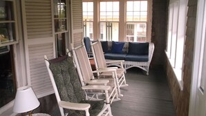 Une véranda aménagée avec des meubles en osier, notamment un canapé et des fauteuils, ainsi qu’une lampe.