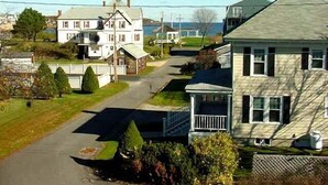 Une rue résidentielle bordée de maisons, un ciel dégagé et une étendue d’eau visible au loin.