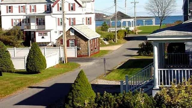 Une maison à deux étages avec un porche, un petit bâtiment indépendant et une vue sur la mer.