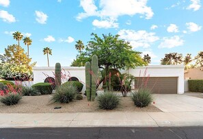A residential area with a white house, a garage, and a well-maintained garden with various cacti and shrubs. - Casa De Sol (Scottsdale)