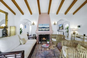 A spacious living room with a fireplace, white walls, wooden beams, and comfortable seating. - Cardillo 3 (Palm Springs)