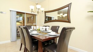Une salle à manger avec une grande table en bois, dressée pour six personnes, entourée de six chaises en cuir. Un lustre est suspendu au-dessus de la table, et un grand miroir est fixé au mur.