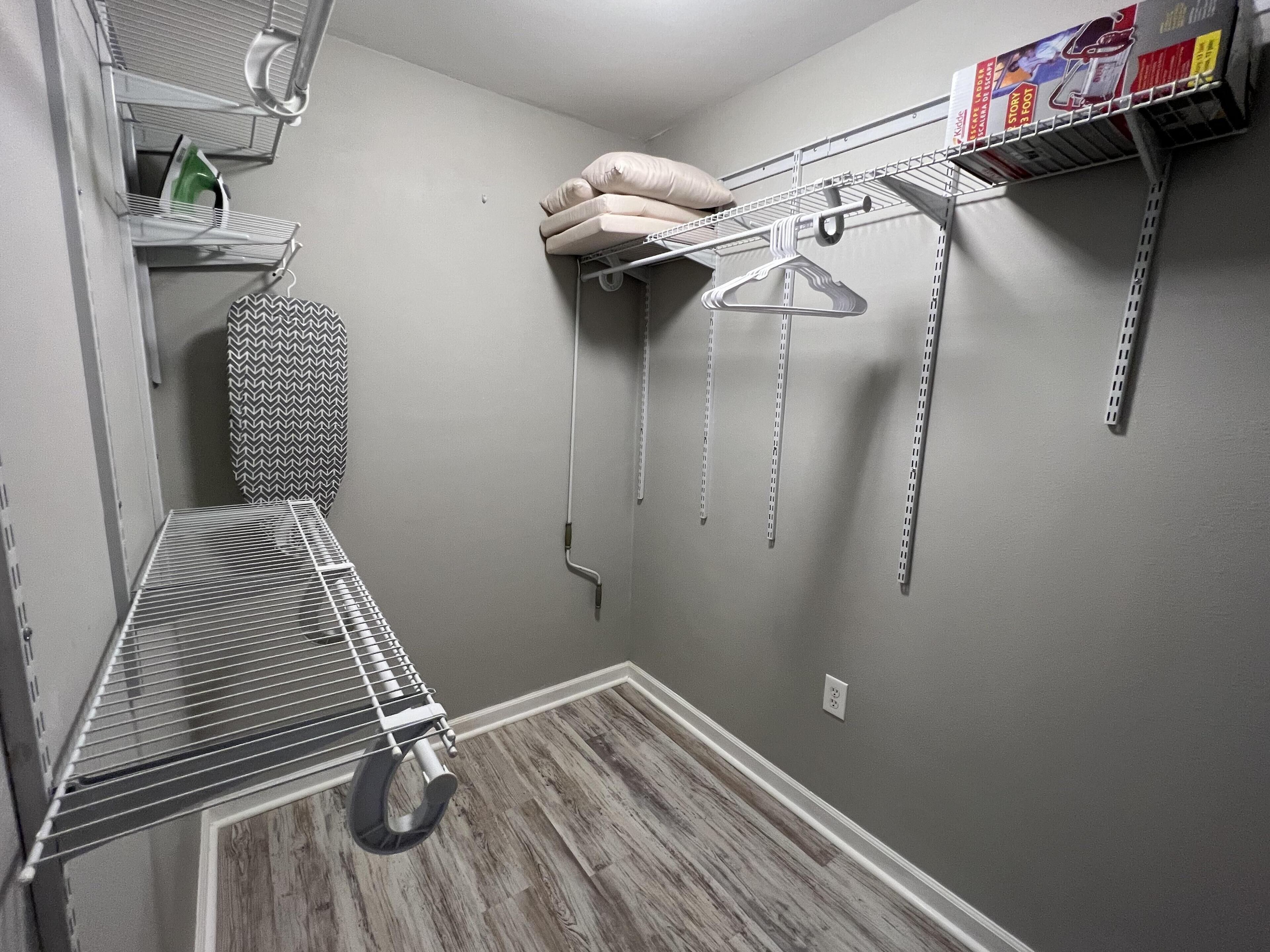 A laundry area with a drying rack, shelves with laundry supplies, and hanging clothes on a rack.