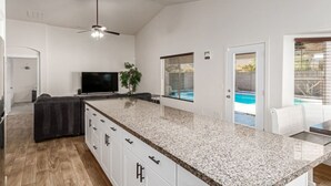 A modern kitchen with a granite countertop, white cabinets, and a built-in TV. - Beautifully Decorated Homeavondaleprivatepool (Avondale)