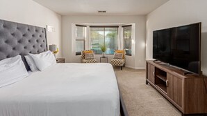 A bedroom with a large bed, a TV, a small seating area, and a window with blinds. - Beautifully Decorated Homeavondaleprivatepool (Avondale)