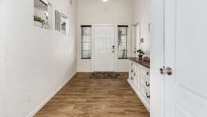 A hallway with wooden flooring, white walls, a white door, and a hanging light fixture. - Beautifully Decorated Homeavondaleprivatepool (Avondale)