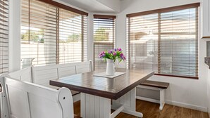 A dining area with a wooden table and white chairs, large windows with blinds, and a vase with flowers on the table. - Beautifully Decorated Homeavondaleprivatepool (Avondale)