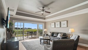 A spacious living room with a large window, a ceiling fan, and a leather sofa. - Di0103 Centre Court Amore (Kissimmee)
