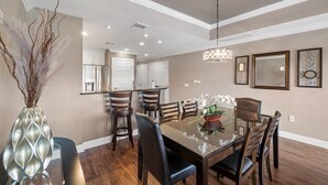 A dining room with a glass table, wooden chairs, a vase with dried branches, and a chandelier. - Di0103 Centre Court Amore (Kissimmee)