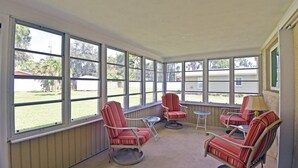 A sunroom with large windows, three striped chairs, a small table, and a lamp. - Beechwood Villa (Sarasota)