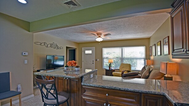 A kitchen with a central island, bar stools, a ceiling fan, and a dining area with a couch and table. - Beechwood Villa (Sarasota)