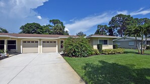 A two-story house with a garage, a well-maintained lawn, and mature trees in the background. - Beechwood Villa (Sarasota)