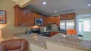 A kitchen with granite countertops, stainless steel appliances, wooden cabinets, and a brown leather chair. - Beechwood Villa (Sarasota)