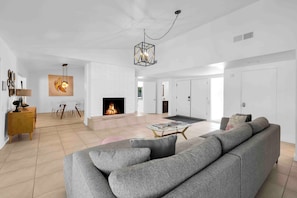 A modern living room with a grey sectional sofa, a glass coffee table, and a fireplace. - Avery (Palm Springs)