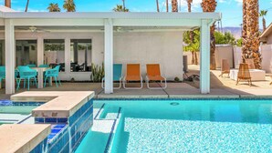 A pool area with lounge chairs, a covered seating area, and a view of palm trees. - Avery (Palm Springs)