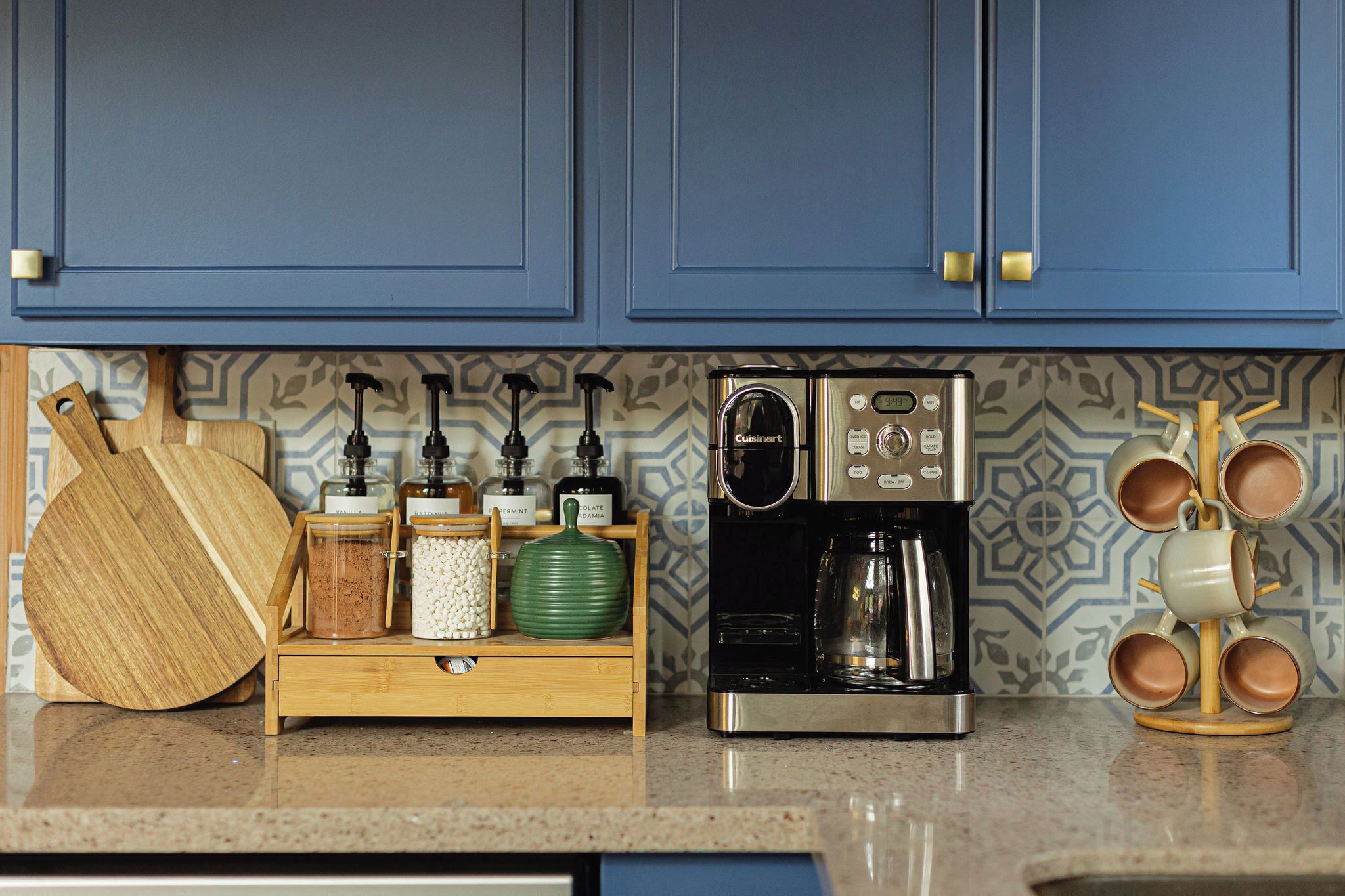 A kitchen with blue cabinets, a coffee maker, a wooden cutting board, and a mug rack.