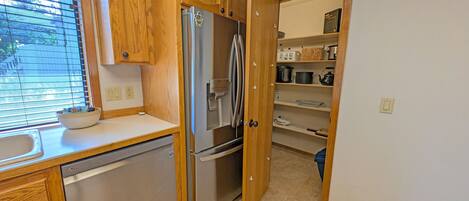 A compact kitchen with wooden cabinets, a stainless steel refrigerator, and a dishwasher.