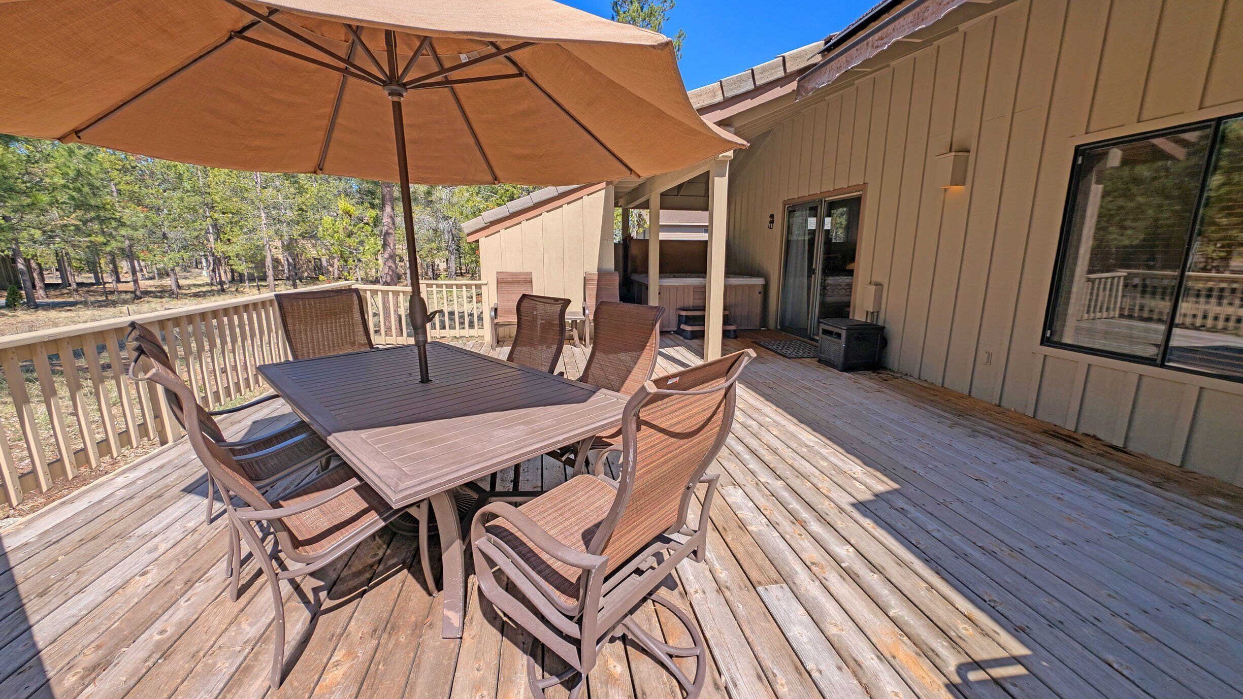 A wooden deck with a table and chairs, a large umbrella, and a building with a glass door.