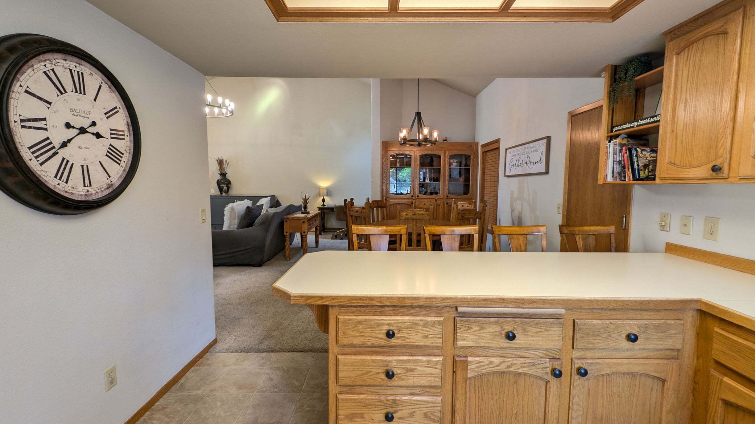 Una cocina con armarios de madera, un reloj y un comedor con candelabro.