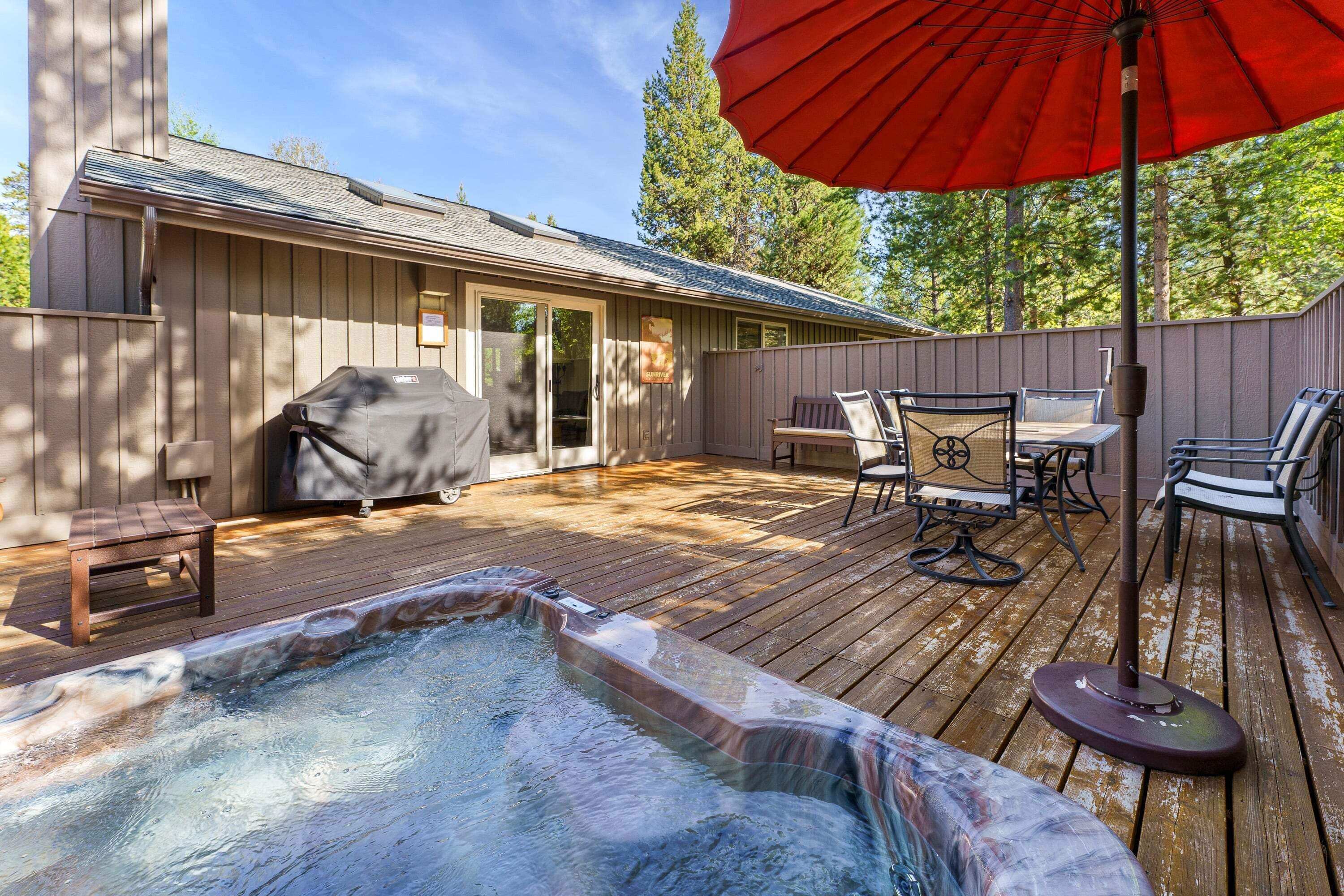 A hot tub on a wooden deck with a barbecue, outdoor furniture, and a covered patio area.