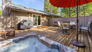 Vasca idromassaggio su un pontile in legno con barbecue, mobili da esterno e una zona patio coperta.