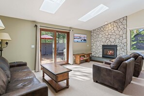 Ein Wohnzimmer mit Kamin aus Stein, Ledersofas, einem Couchtisch und einer Glastür, die zu einem Außenbereich führt.