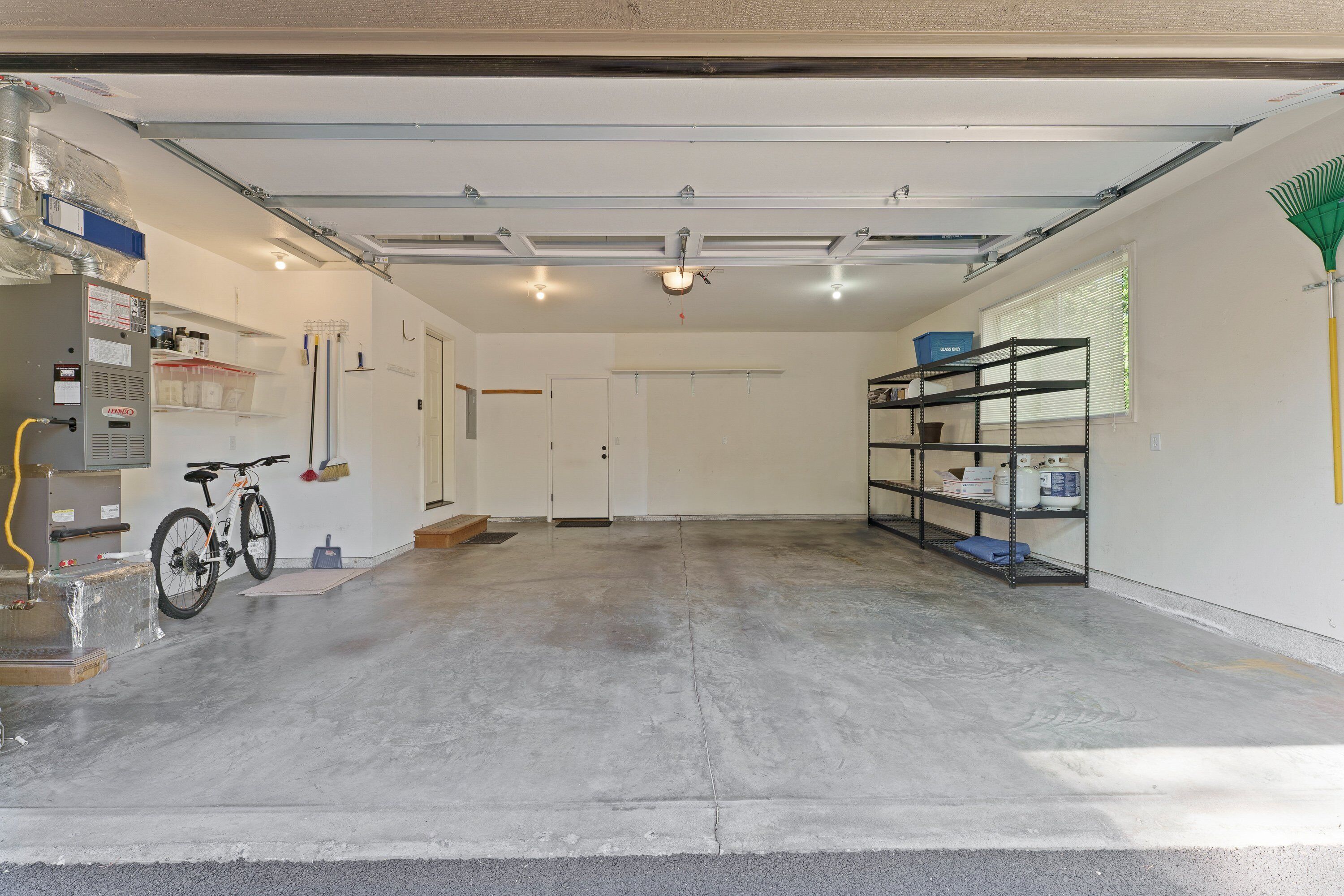 Garagem limpa e bem iluminada, com piso de concreto, uma bicicleta e prateleiras com diversos objetos.