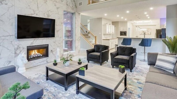 A spacious living area with a fireplace, comfortable seating, a TV, and a kitchen in the background.