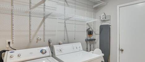 A laundry room with two washers and dryers, metal shelving, a drying rack, and a door with a 'MOM' sign.