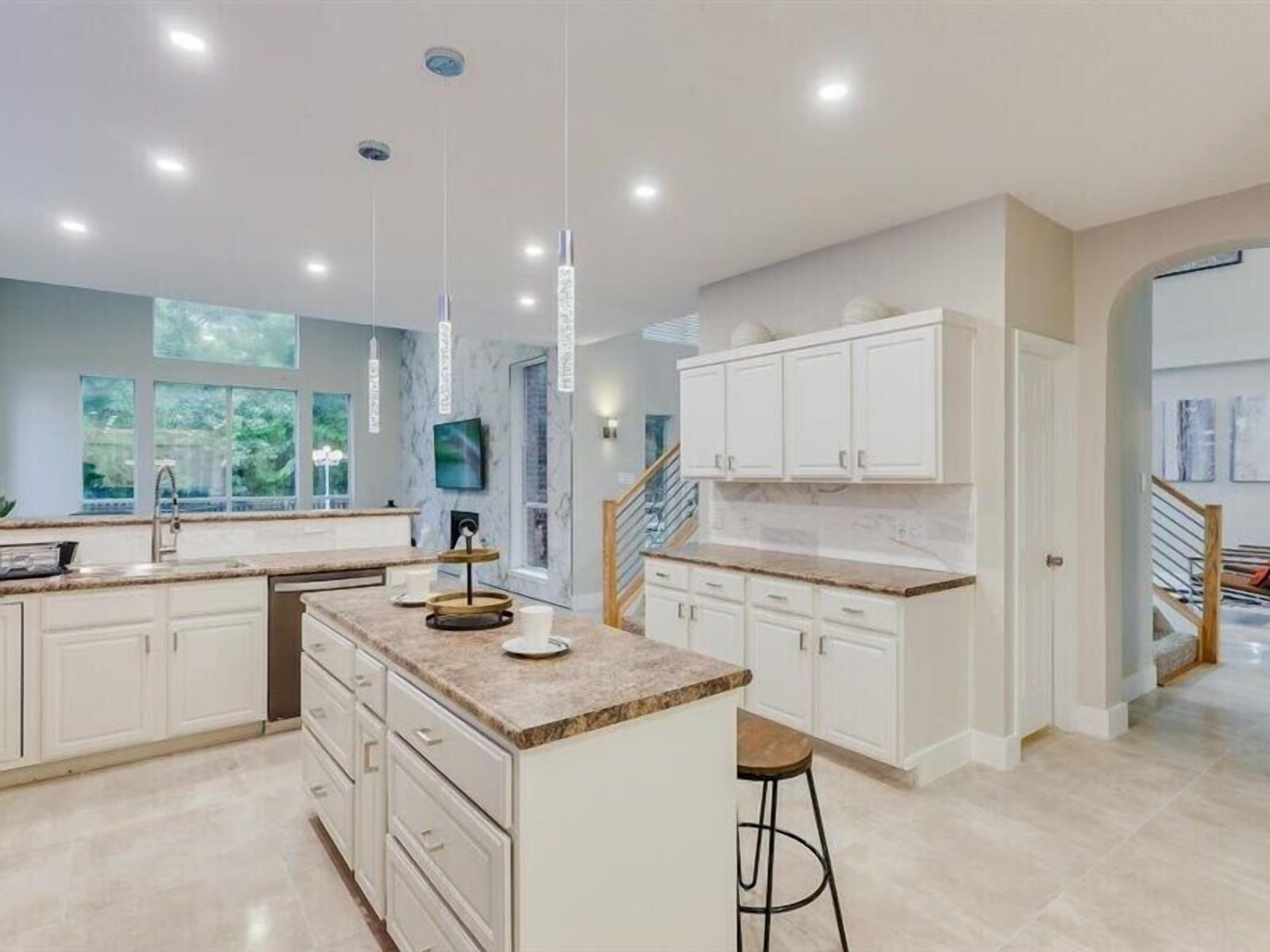 A modern kitchen with white cabinetry, a marble countertop, and pendant lighting.