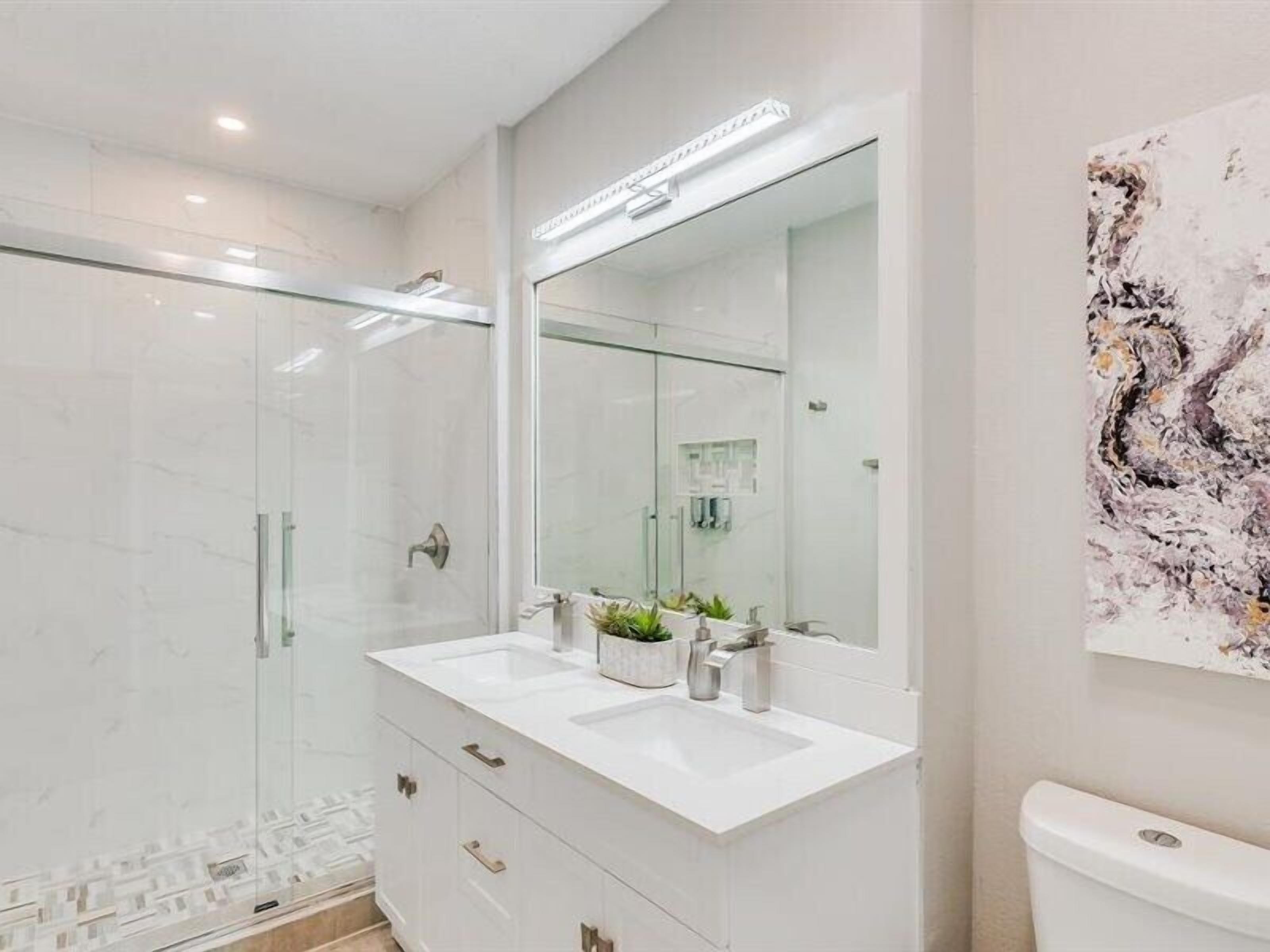 A modern bathroom with a glass shower enclosure, a white vanity with a large mirror, and a toilet.