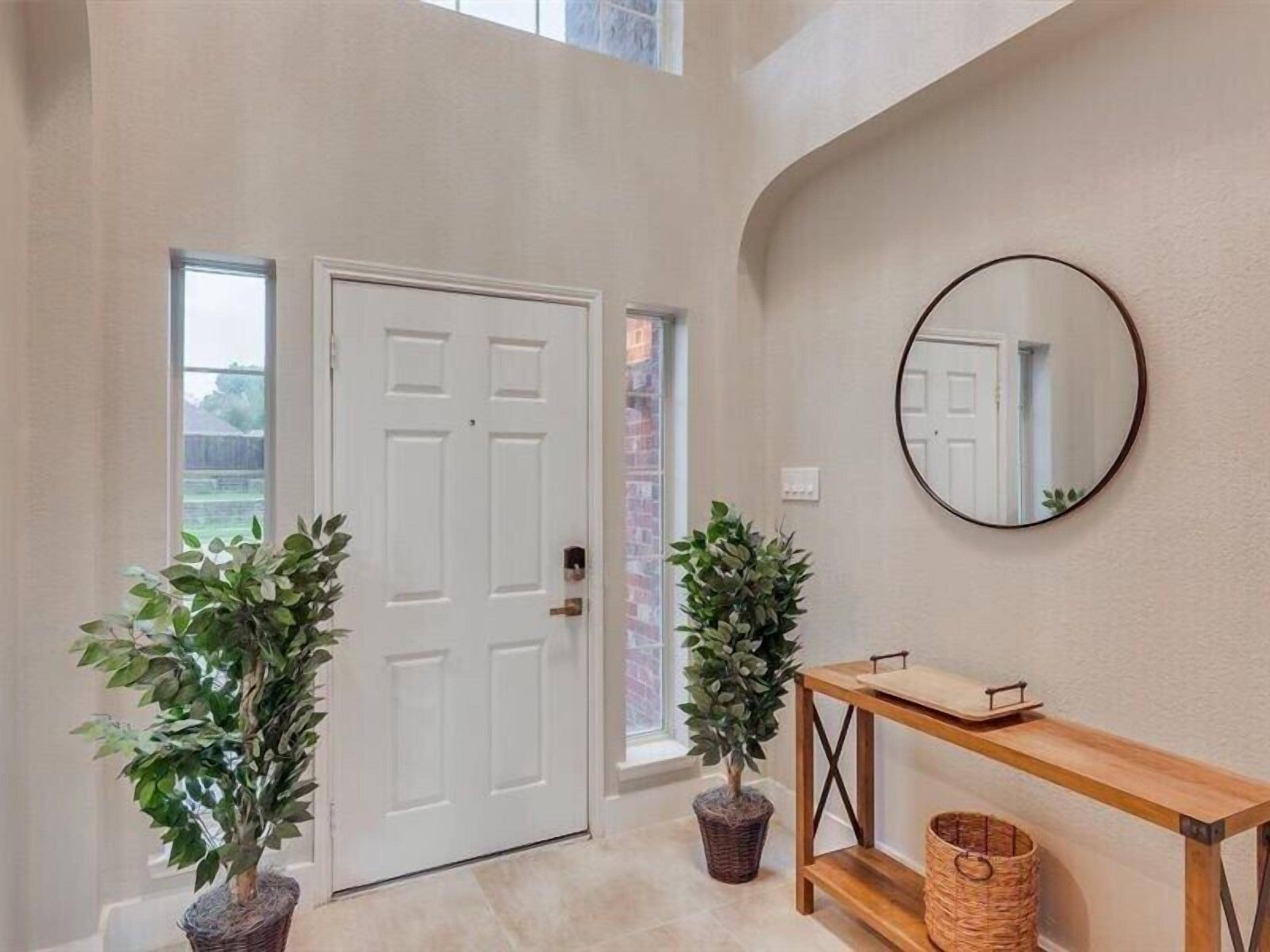 A hallway with a white door, a round mirror on the wall, and two potted plants.
