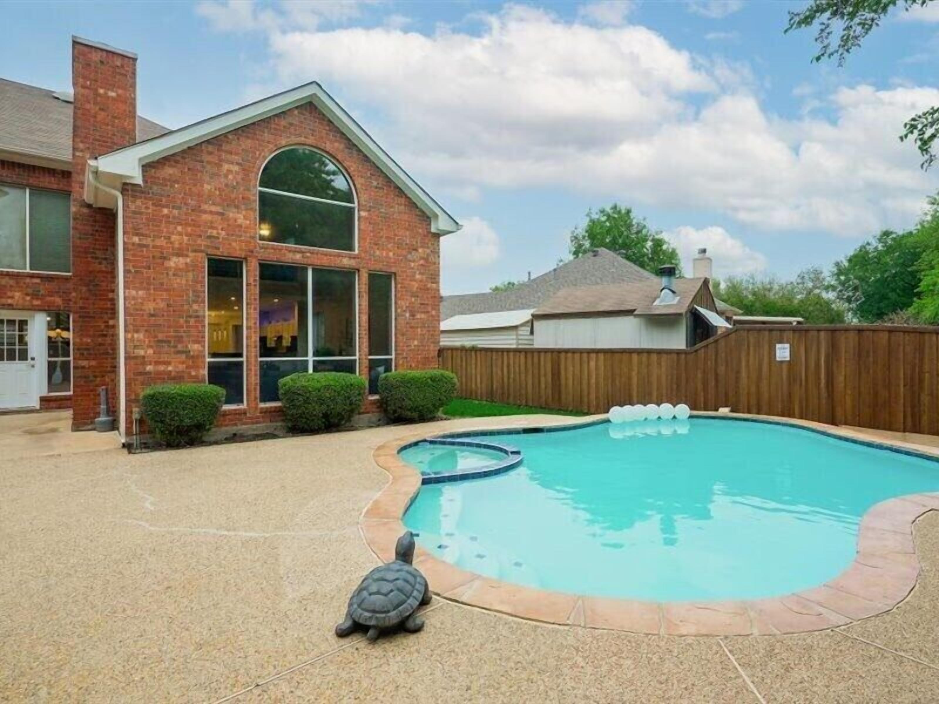 Un patio trasero residencial con piscina, una casa de ladrillo y una valla de madera.